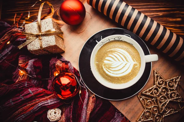 Ahşap arka planda bir fincan kahve, içinde Noel oyuncakları ve kağıt var.