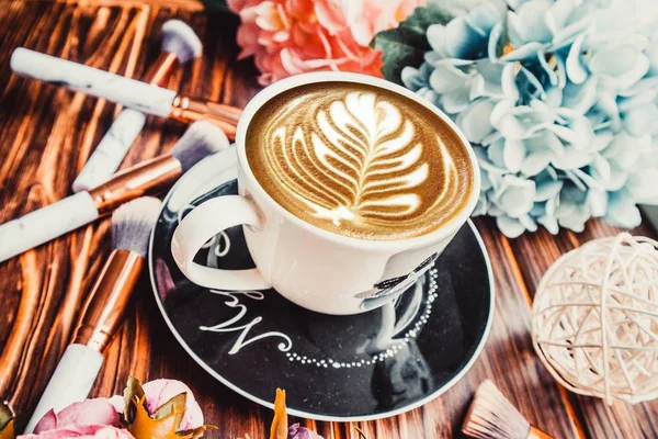 Kahverengi Arka Planda Çiçekli Makyaj Fırçalı Bir Fincan Kahve — Stok fotoğraf