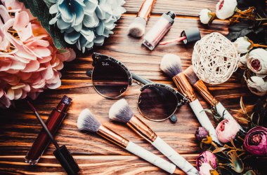 Kahverengi ahşap arka planda çiçekler ve makyaj fırçaları.