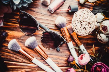 Kahverengi ahşap arka planda çiçekler ve makyaj fırçaları.