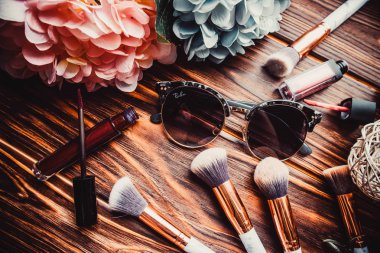 Kahverengi ahşap arka planda çiçekler ve makyaj fırçaları.