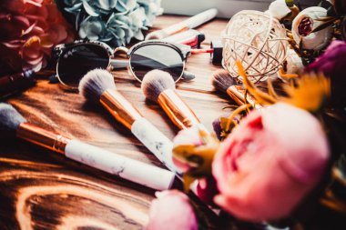 Kahverengi ahşap arka planda çiçekler ve makyaj fırçaları.