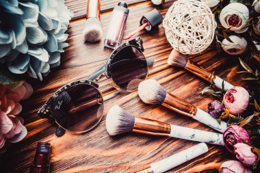 Kahverengi ahşap arka planda çiçekler ve makyaj fırçaları.