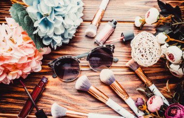 Kahverengi ahşap arka planda çiçekler ve makyaj fırçaları.