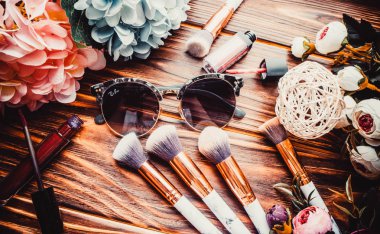 Kahverengi ahşap arka planda çiçekler ve makyaj fırçaları.