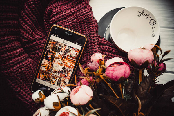 Phone and cup on soft sweater and white wooden background