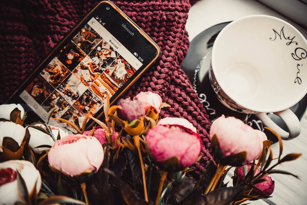 Phone and cup on soft sweater and white wooden background