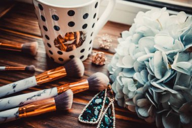 Bir fincan kahve, makyaj fırçaları ve çiçekler ahşap kahverengi arka planda.