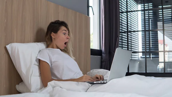 nice girl works on computer sitting in bed, work during weekend, laptop on legs,