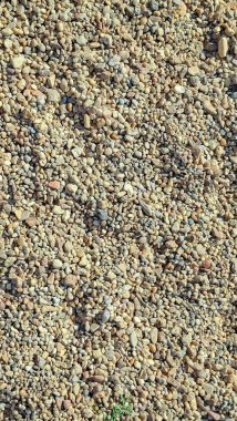 Çeşitli boyutlarda çakıl ve taş içeren çakıl taşı yüzeyinin yakın görüntüsü.