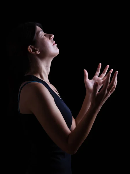 一个忠实的女人祈祷和感受上帝的存在或被感动的低调 在崇拜中张开双臂 在宗教狂热中闭上眼睛 黑色背景 — 图库照片