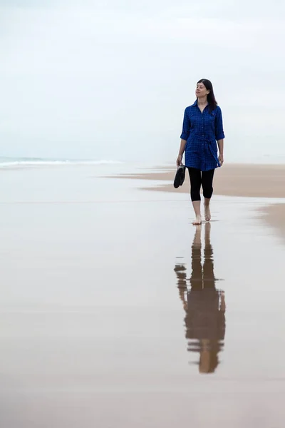 在一个荒凉的海滩上独自行走的年轻女子 在秋天的潮湿的沙滩上反射 — 图库照片