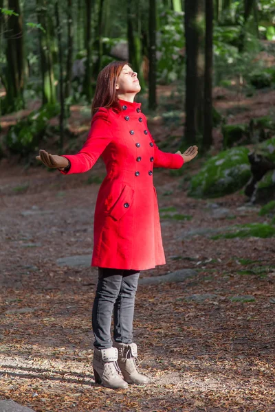 女性の赤いコートを着て森の冬の日光の暖かさを楽しんで — ストック写真