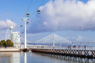 Lisbon, Portugal - February 01, 2015: People practicing sports on the Passeio Ribeirinho over the Tagus River. Vasco da Gama Tower and Bridge, Myriad Hotel and aerial tramway. Park of Nations clipart