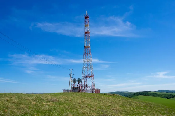 Mavi gökyüzüne karşı bir tepenin üstünde telefon iletişim kulesi.