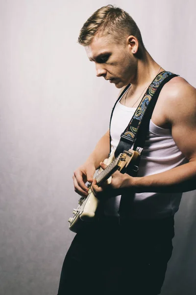 Musician playing music. Modern style guitar player. Man with electric guitar. Portrait of adult musician playing instrument. Young muscular man in casual clothes playing guitar on gray background.