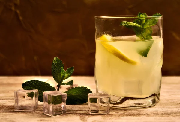 Üzerinde düz cam Limonata limon, buz küpleri ve içinde nane ve buz küpleri ve nane sol tarafındaki ağaç ve kahverengi arka plan üzerinde resmi