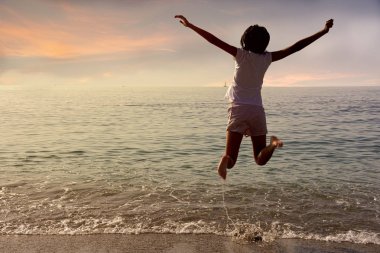 gün batımında denizin önünde atlayan küçük kız