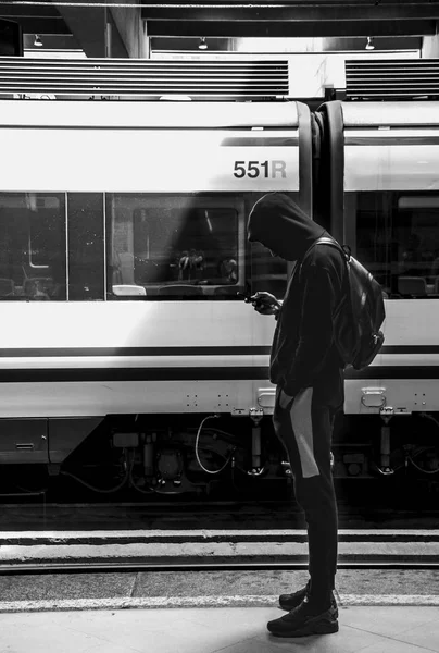 Jovem olhando para o telefone e enquanto espera o trem — Fotografia de Stock