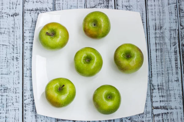 Green fresh apples on a white plate on a wooden table close-up, rustic style