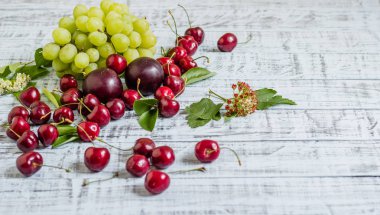 büyük tatlı sulu kiraz, Erik ve üzüm, yapraklar ve çiçekler ahşap arka plan, sağlıklı beslenme kavramı üzerinde