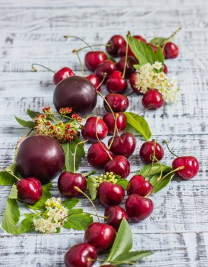 büyük tatlı sulu kiraz, Erik ve üzüm, yapraklar ve çiçekler ahşap arka plan, sağlıklı beslenme kavramı üzerinde