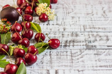 büyük tatlı sulu kiraz, Erik ve üzüm, yapraklar ve çiçekler ahşap arka plan, sağlıklı beslenme kavramı üzerinde