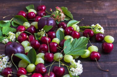 büyük tatlı sulu kiraz, Erik ve üzüm, yapraklar ve çiçekler ahşap arka plan, sağlıklı beslenme kavramı üzerinde