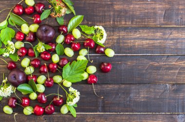 büyük tatlı sulu kiraz, Erik ve üzüm, yapraklar ve çiçekler ahşap arka plan, sağlıklı beslenme kavramı üzerinde