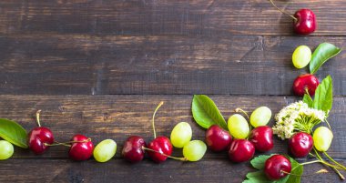 Olgun kiraz yaprakları, üzüm ve çiçek bir ahşap tahta üzerinde bir bahçeden bir çerçeve. Yukarıdan görüntülemek