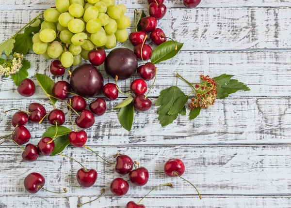 büyük tatlı sulu kiraz, Erik ve üzüm, yapraklar ve çiçekler ahşap arka plan, sağlıklı beslenme kavramı üzerinde