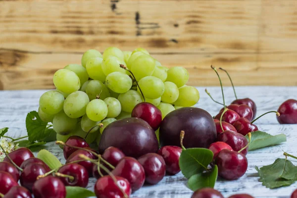 büyük tatlı sulu kiraz, Erik ve üzüm, yapraklar ve çiçekler ahşap arka plan, sağlıklı beslenme kavramı üzerinde