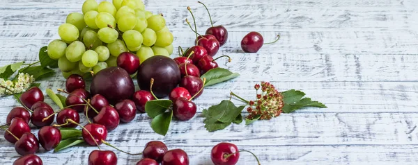 büyük tatlı sulu kiraz, Erik ve üzüm, yapraklar ve çiçekler ahşap arka plan, sağlıklı beslenme kavramı üzerinde