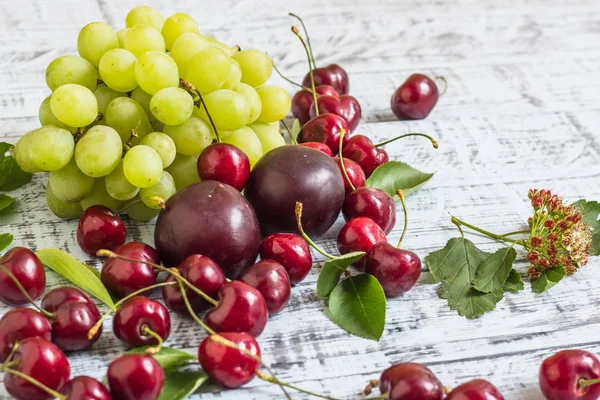 büyük tatlı sulu kiraz, Erik ve üzüm, yapraklar ve çiçekler ahşap arka plan, sağlıklı beslenme kavramı üzerinde