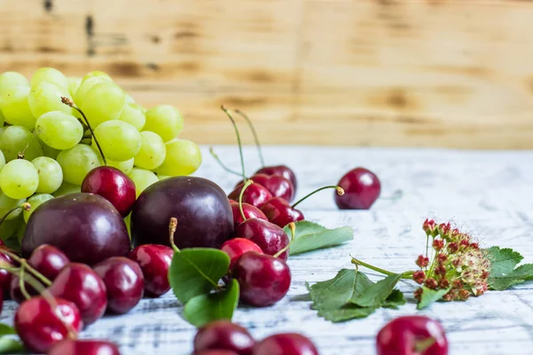 büyük tatlı sulu kiraz, Erik ve üzüm, yapraklar ve çiçekler ahşap arka plan, sağlıklı beslenme kavramı üzerinde