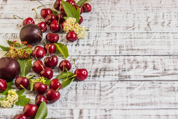 büyük tatlı sulu kiraz, Erik ve üzüm, yapraklar ve çiçekler ahşap arka plan, sağlıklı beslenme kavramı üzerinde