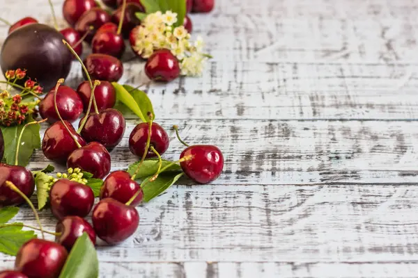 büyük tatlı sulu kiraz, Erik ve üzüm, yapraklar ve çiçekler ahşap arka plan, sağlıklı beslenme kavramı üzerinde