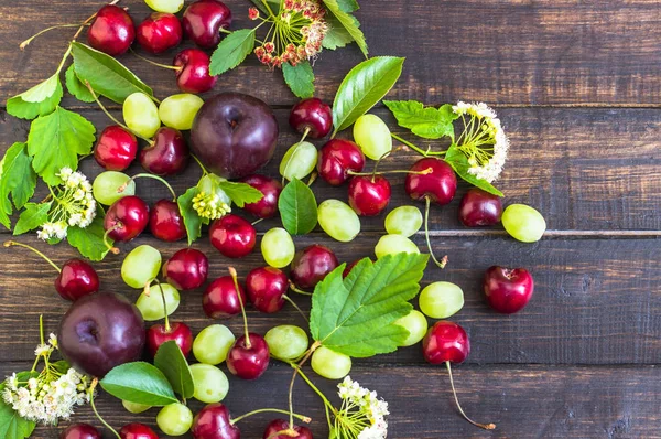 büyük tatlı sulu kiraz, Erik ve üzüm, yapraklar ve çiçekler ahşap arka plan, sağlıklı beslenme kavramı üzerinde