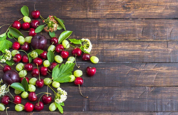 büyük tatlı sulu kiraz, Erik ve üzüm, yapraklar ve çiçekler ahşap arka plan, sağlıklı beslenme kavramı üzerinde