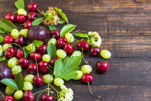 büyük tatlı sulu kiraz, Erik ve üzüm, yapraklar ve çiçekler ahşap arka plan, sağlıklı beslenme kavramı üzerinde