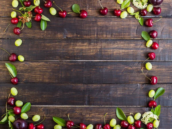 Olgun kiraz yaprakları, üzüm ve çiçek bir ahşap tahta üzerinde bir bahçeden bir çerçeve. Yukarıdan görüntülemek