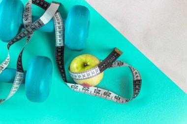 Turkuaz dambıl, teyp ve apple parlak turkuaz arka plan üzerinde ölçüm. Sağlıklı yaşam, vücut kilo kaybı kavramı. Vücudu hakkında umurunda. Metin için boş yer.