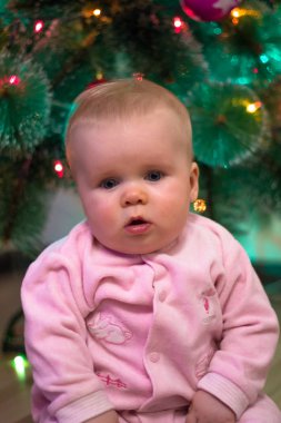 Pembe Tulum, küçük bir kız Noel ağacı arka plan üzerinde oturuyor. Yılbaşı tatil. Noel tatili.