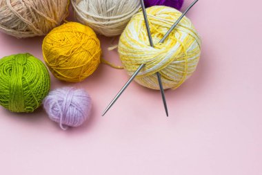 Products for needlework, knitting. Balls of yellow, green, purple yarn, knitting needles on a pink background. Space for text. clipart