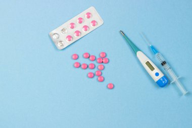 İlaçlar. Elektronik termometre, pembe hapları ve şırınga mavi bir arka plan üzerinde