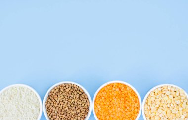 Mavi arka planda çeşitli tahıl gevreği. Karabuğday, mercimek, pirinç, tabak üst görünümü, kopya alanı bezelye