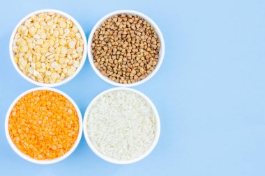 Mavi arka planda çeşitli tahıl gevreği. Karabuğday, mercimek, pirinç, tabak üst görünümü, kopya alanı bezelye