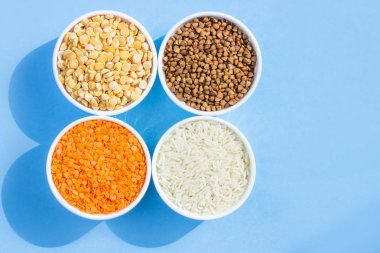 Mavi arka planda çeşitli tahıl gevreği. Karabuğday, mercimek, pirinç, tabak üst görünümü, kopya alanı bezelye
