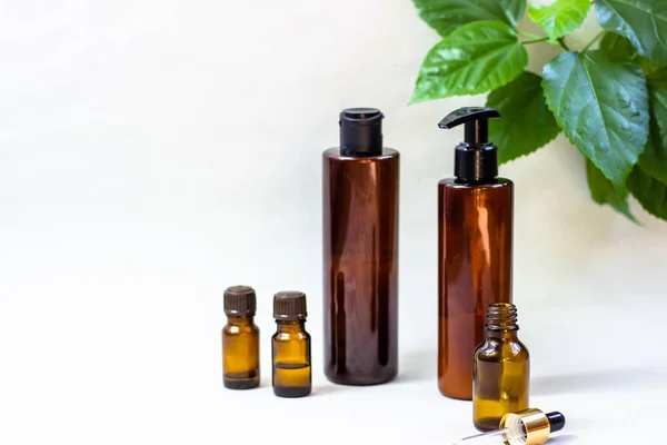 Dark cosmetic bottles and green natural leaves on a light background. Copy space Beauty salon blogger, salon therapy, minimalist concept. The concept of natural environmentally friendly cosmetics. — Stock Photo, Image