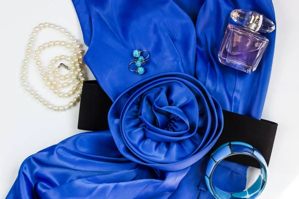 Vestido de mujer azul brillante y accesorios sobre un fondo blanco. Cinturón de flores, collar de perlas, pendientes, pulsera y perfume. Trajes casuales para mujeres. Asiento plano, vista superior. El aspecto a la moda veraniego . — Foto de Stock